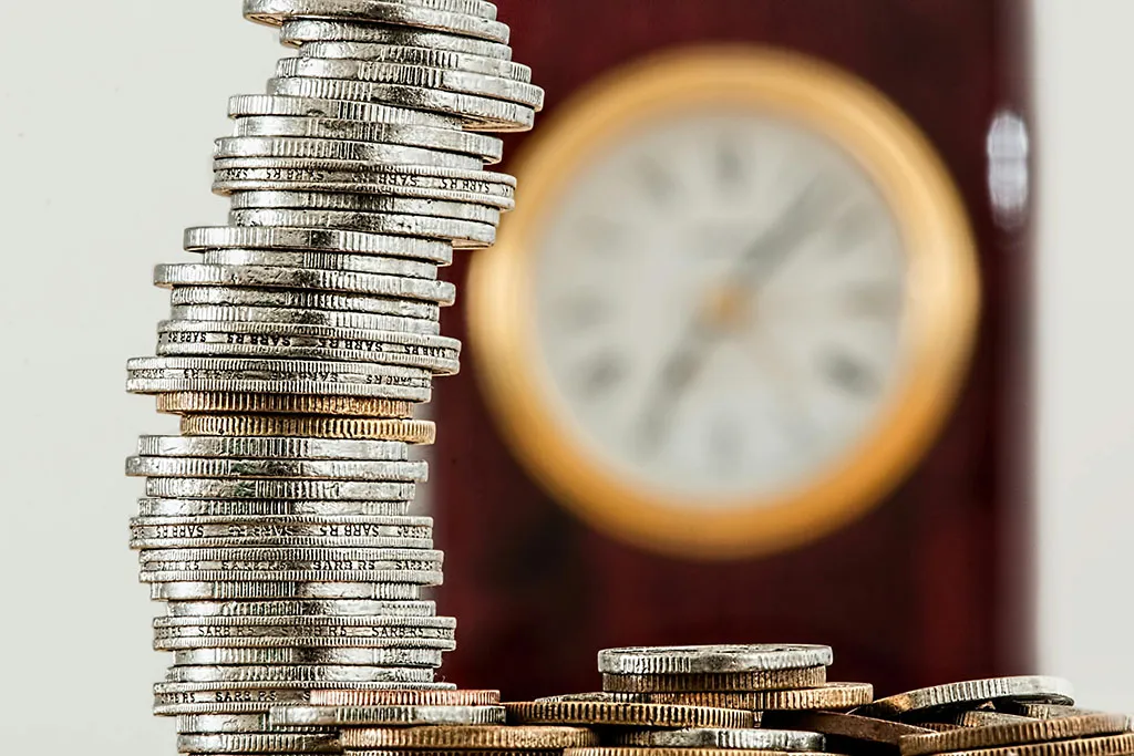 A pile of coins with a clock in the background